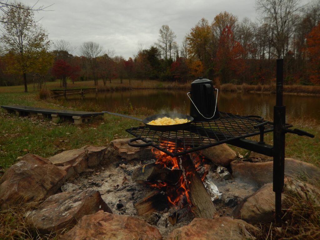 Eggs cooking and coffee percolating on a campfire grill.